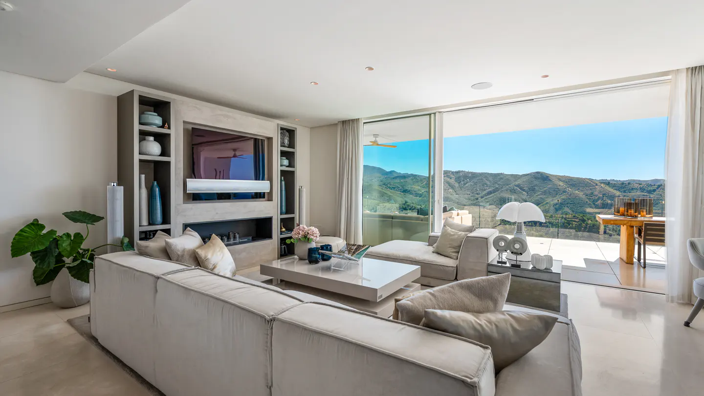 Bright living room with a large white sofa, a TV, and a view of mountains through sliding glass doors.