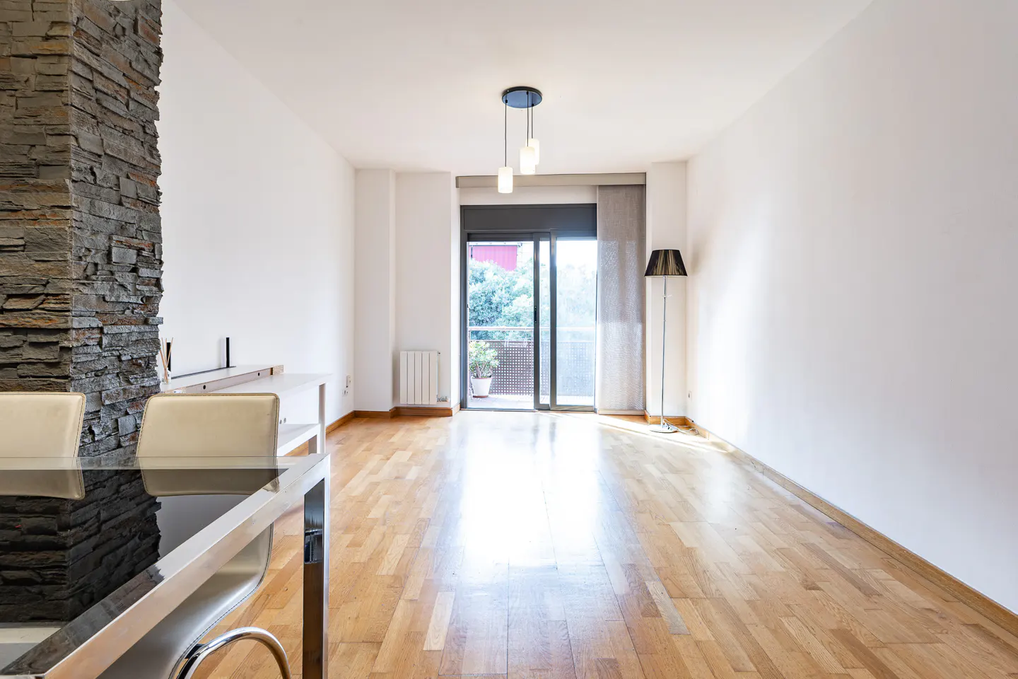 Bright living room with hardwood floors, a stone accent wall, modern pendant lighting, and a balcony door.