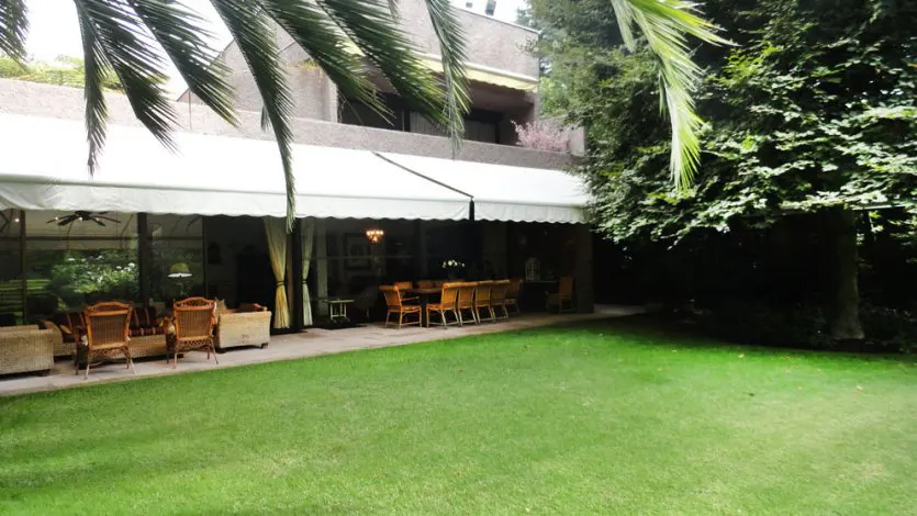 A house with a green lawn and a covered patio with wicker furniture.