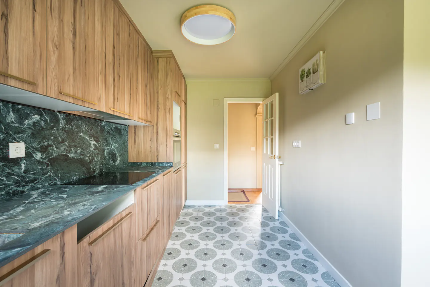 A kitchen with wood cabinets, green marble countertops, and patterned tile floors. A white door is open to another room.