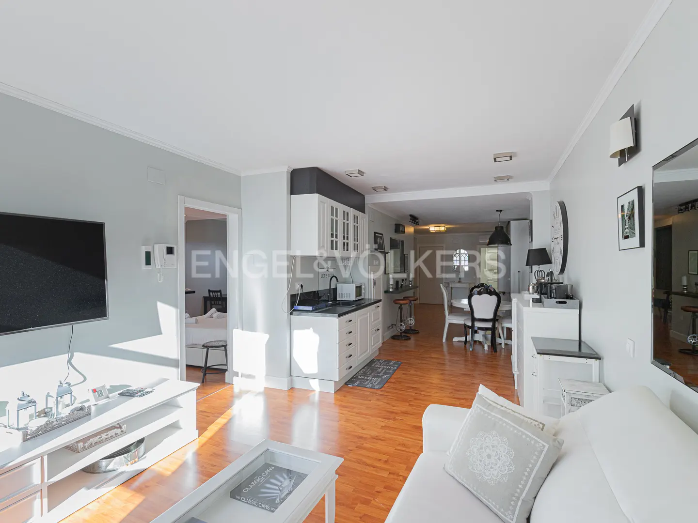 Bright, open-concept living space with hardwood floors, white sofa, and a view into the kitchen and dining area. Engel & Völkers logo visible.