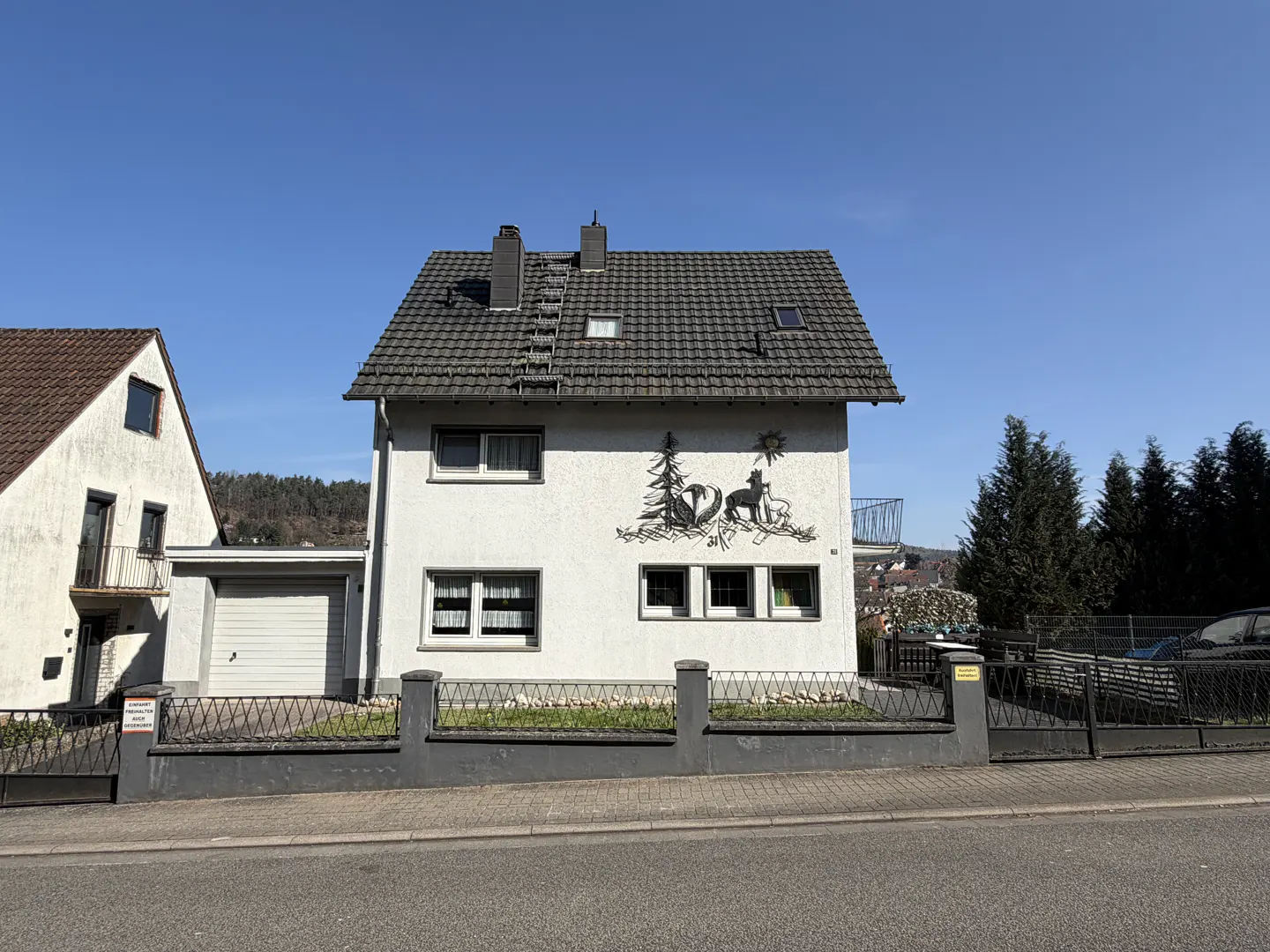 Two-story white house with gray roof and animal mural on the side, surrounded by a gray fence.