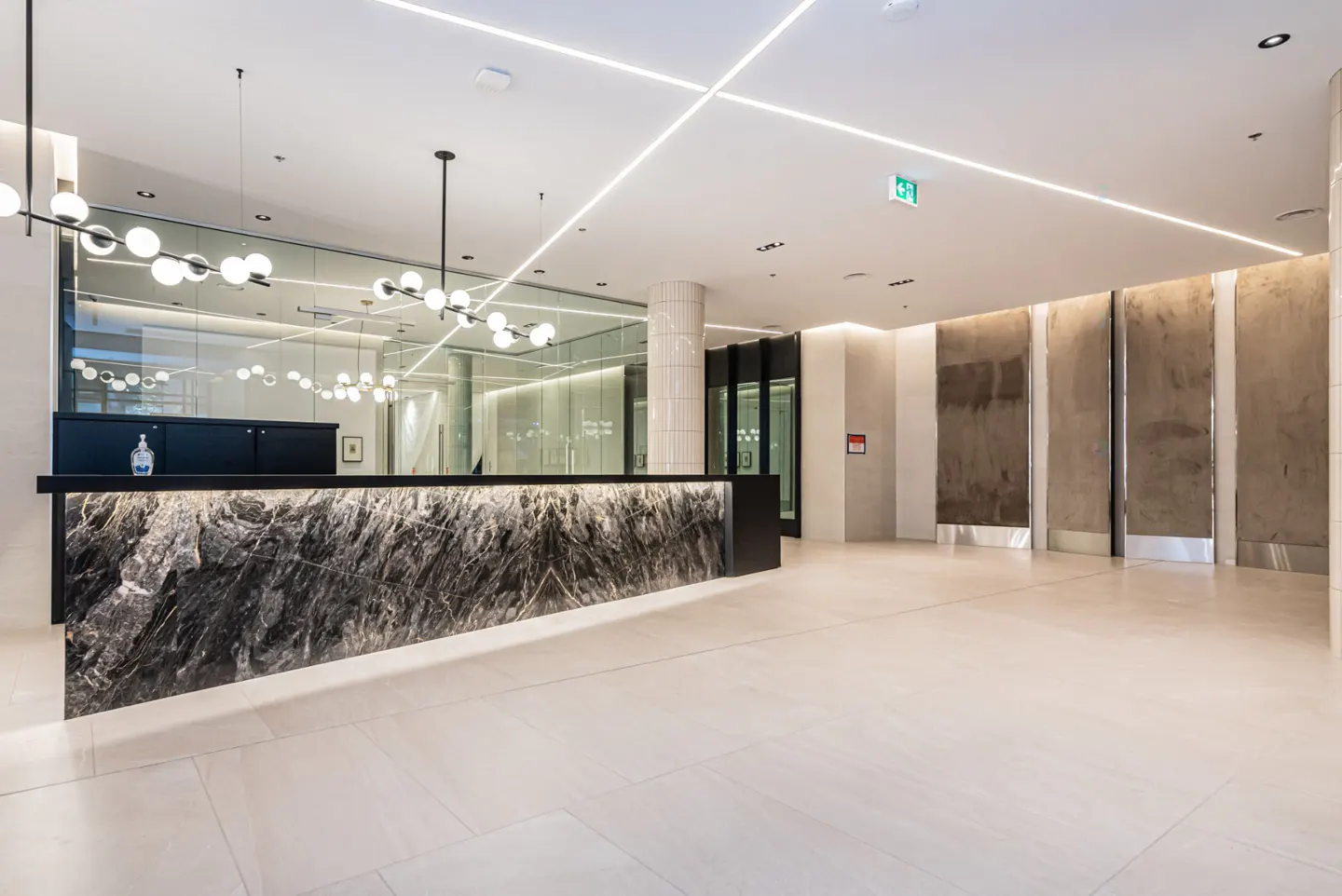 Modern lobby with marble reception desk, globe pendant lights, and light beige tile flooring.
