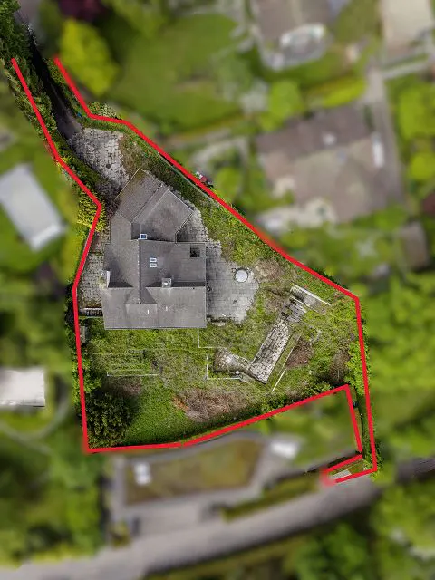 Aerial view of a property with a gray roof house, green lawn, and a red boundary line.
