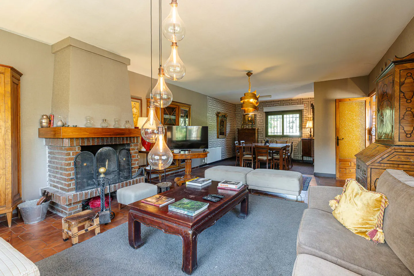 A living room with a brick fireplace, a dark wood coffee table with books, and a gray sofa with a yellow pillow.