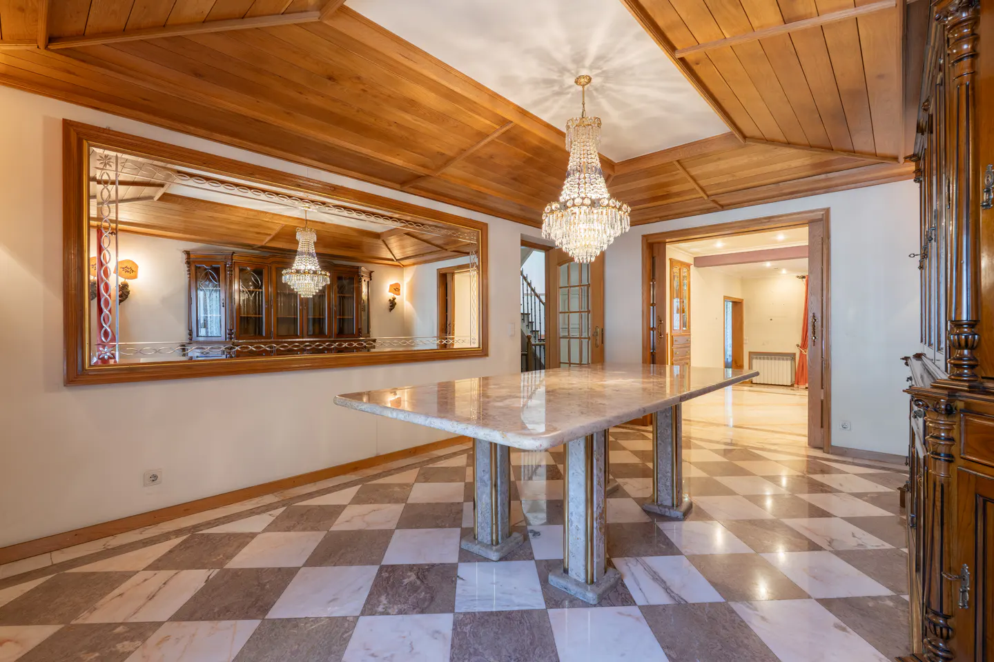 A dining room with a marble table, checkered floor, wood ceiling, and a crystal chandelier.