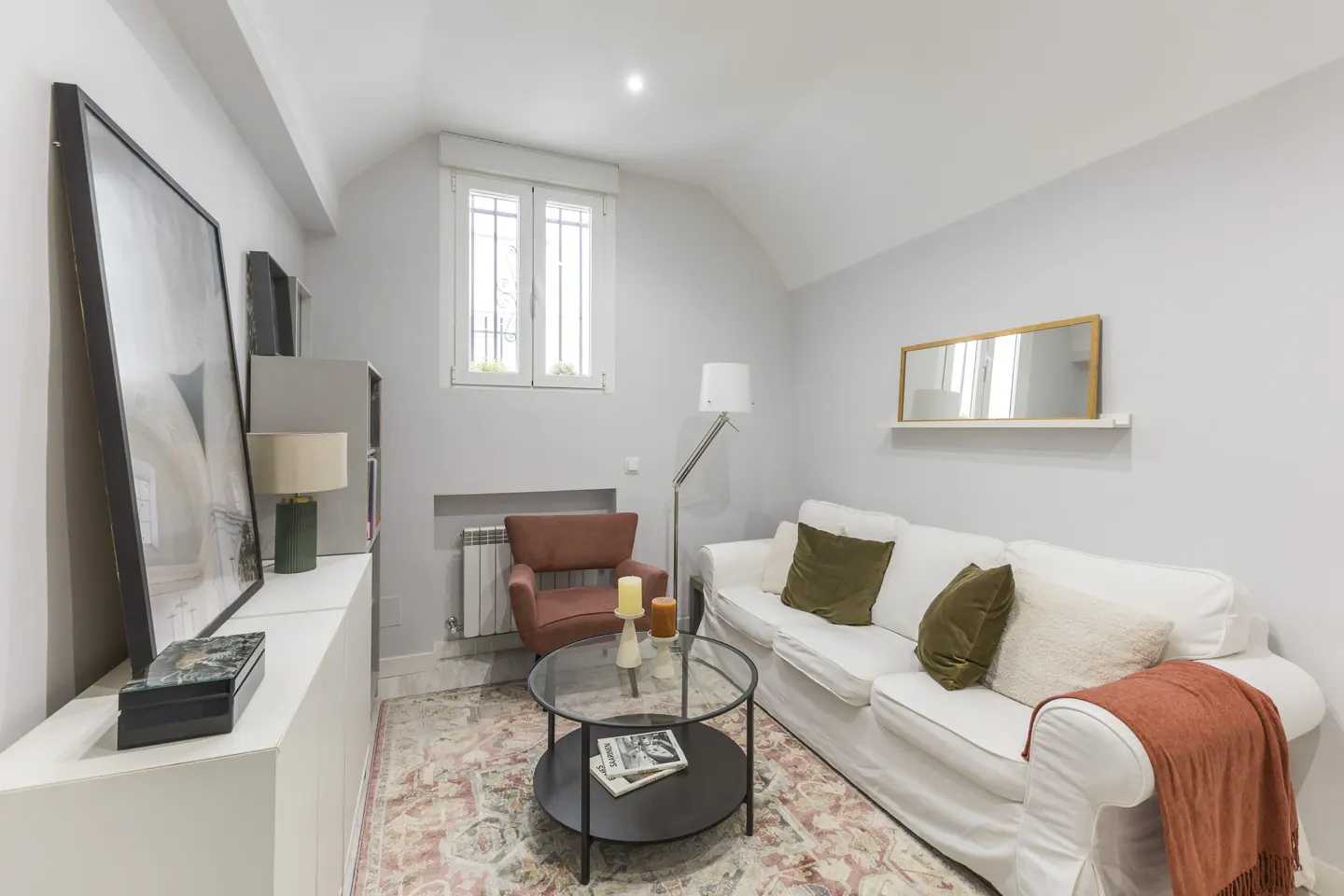 Cozy living room with a white sofa, terracotta armchair, glass coffee table, and a patterned rug on a light gray floor.