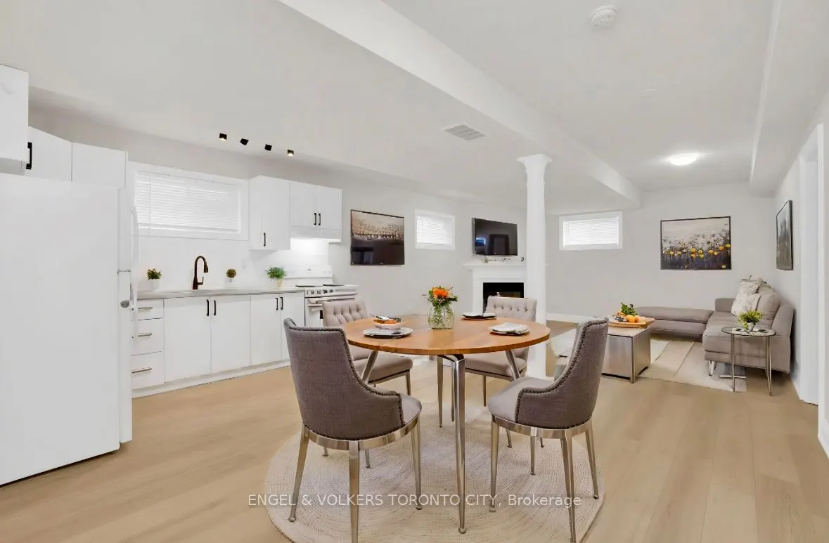 Bright, open-concept living space with white kitchen, dining table, and gray sectional sofa.