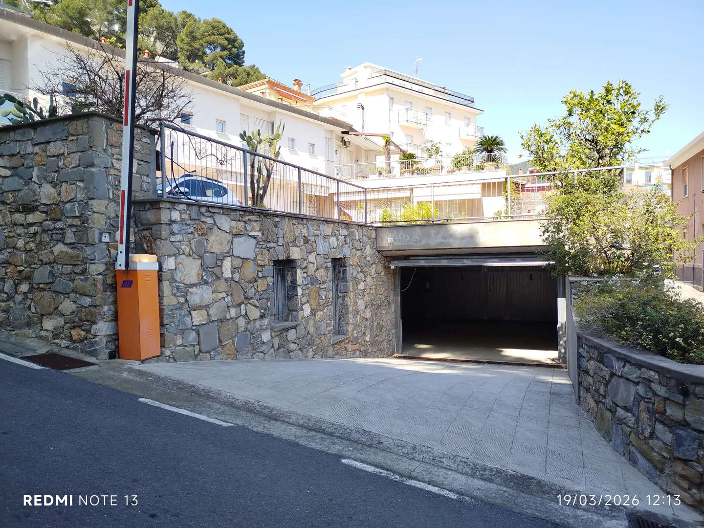 Stone wall with an open garage door and an orange security gate on a sunny day.
