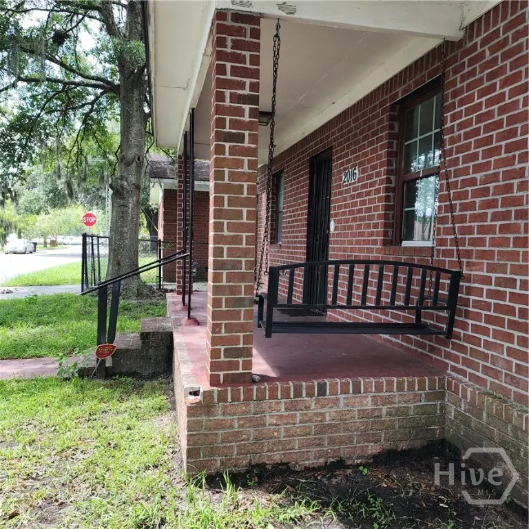 Exterior view of a red brick house with a porch swing hanging from the ceiling. The house number "2016" is visible above the porch.