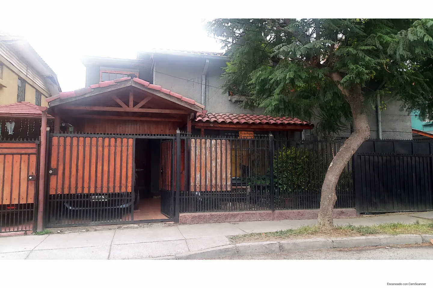 Two-story house with a wooden fence and gate, a red tile roof, and a tree in the front yard.