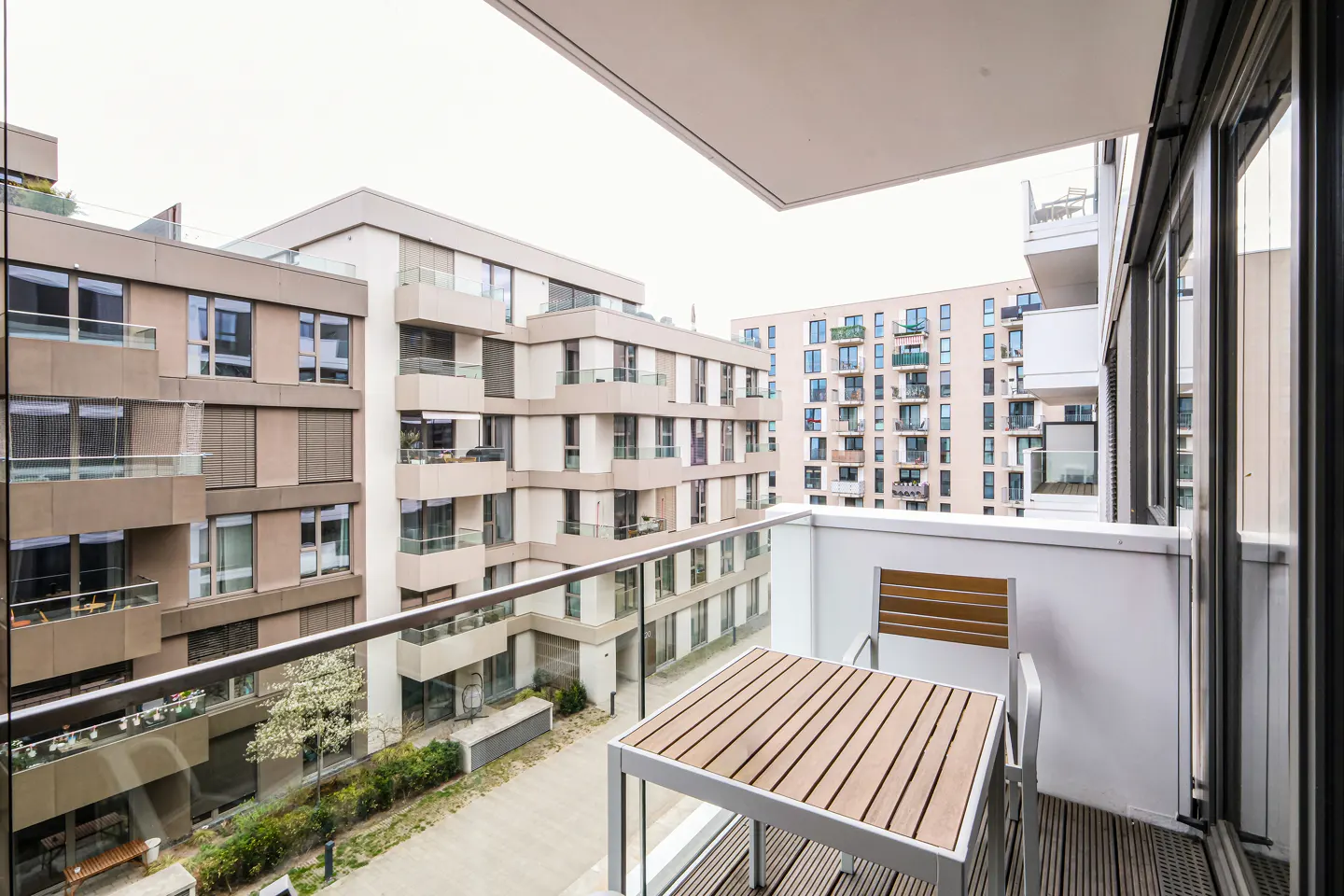 Balcony view with a wooden table and chair set. Buildings are visible in the background.