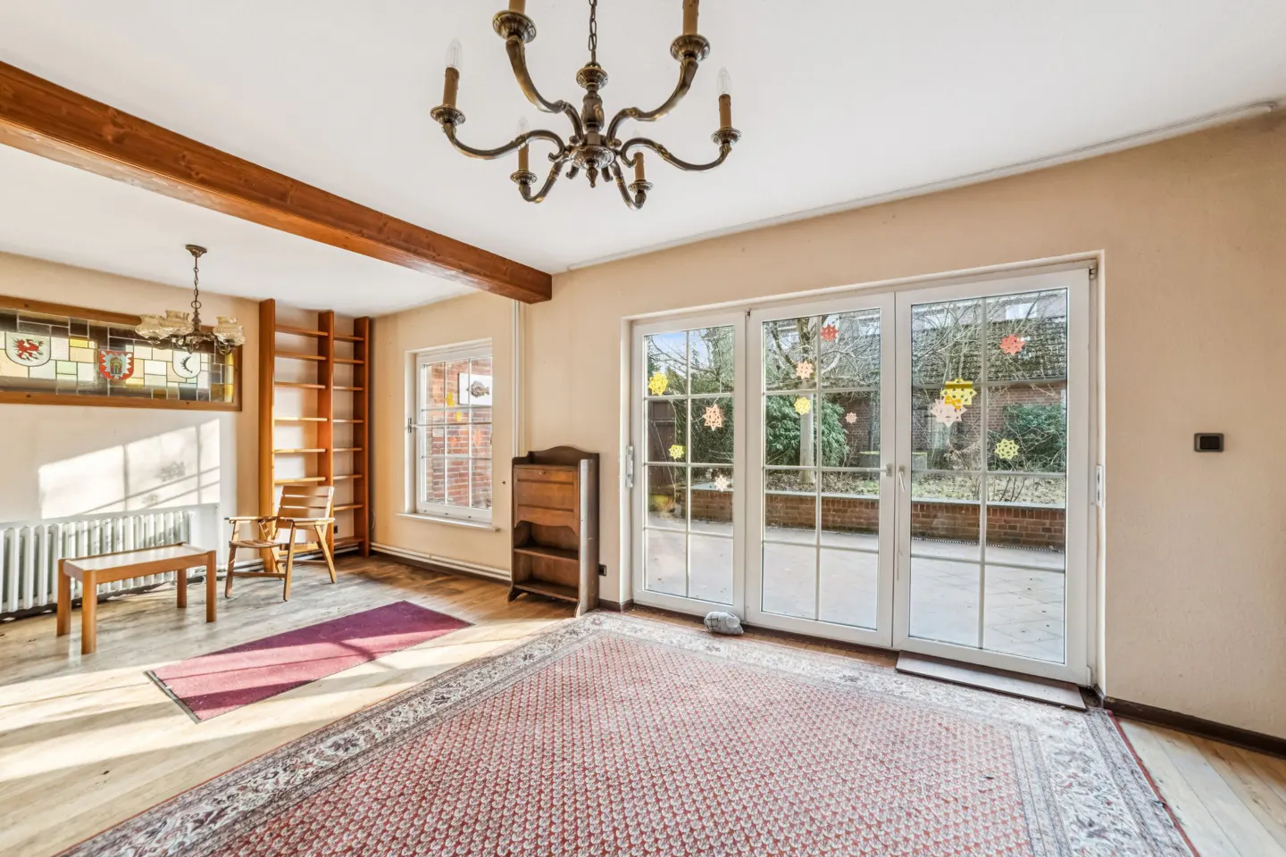 A bright room with a chandelier, a rug, and glass doors to a garden.