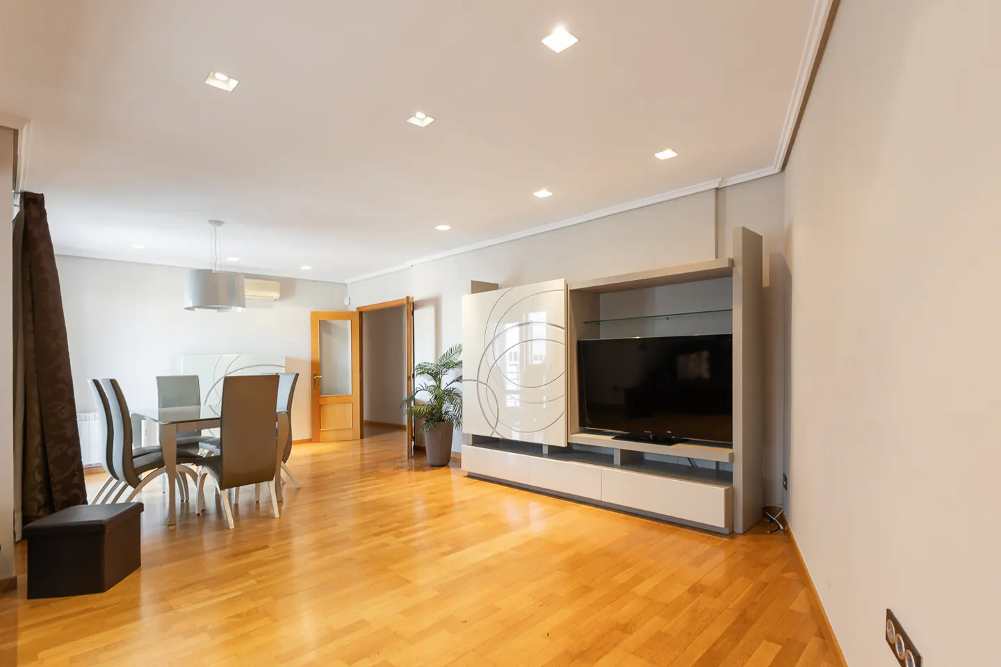 Bright, open-concept living and dining area with hardwood floors. A modern TV stand and dining set are visible. Neutral color palette.