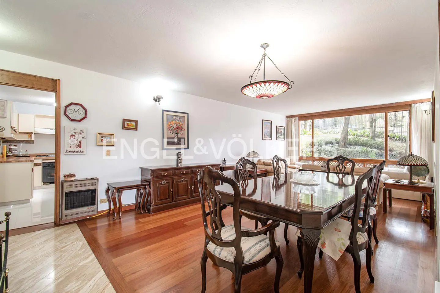 Dining room with dark wood table and chairs, hardwood floors, a large window, and a view into a kitchen.