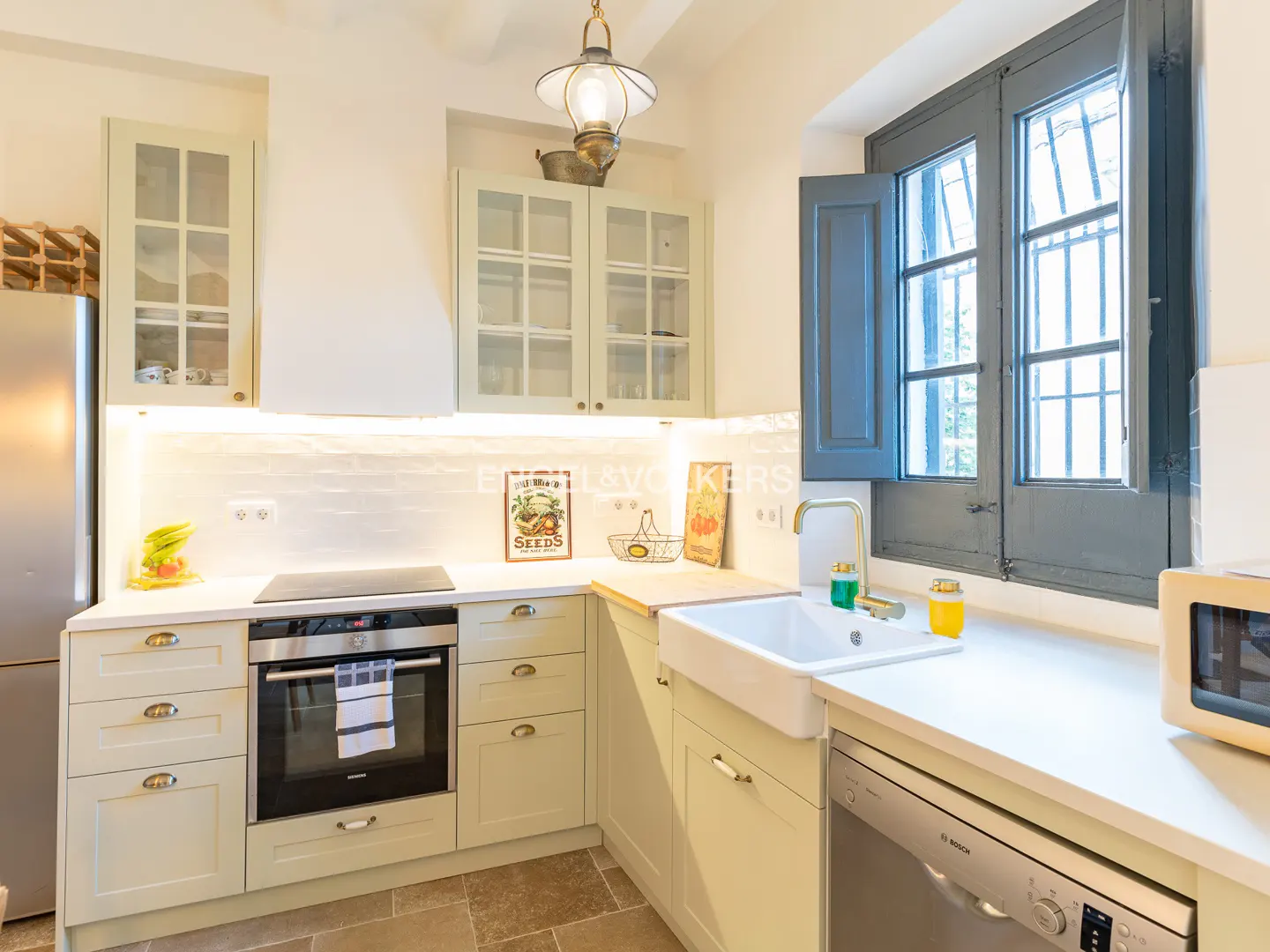 Bright kitchen with sage green cabinets, white countertops, a farmhouse sink, and a window with dark grey shutters.