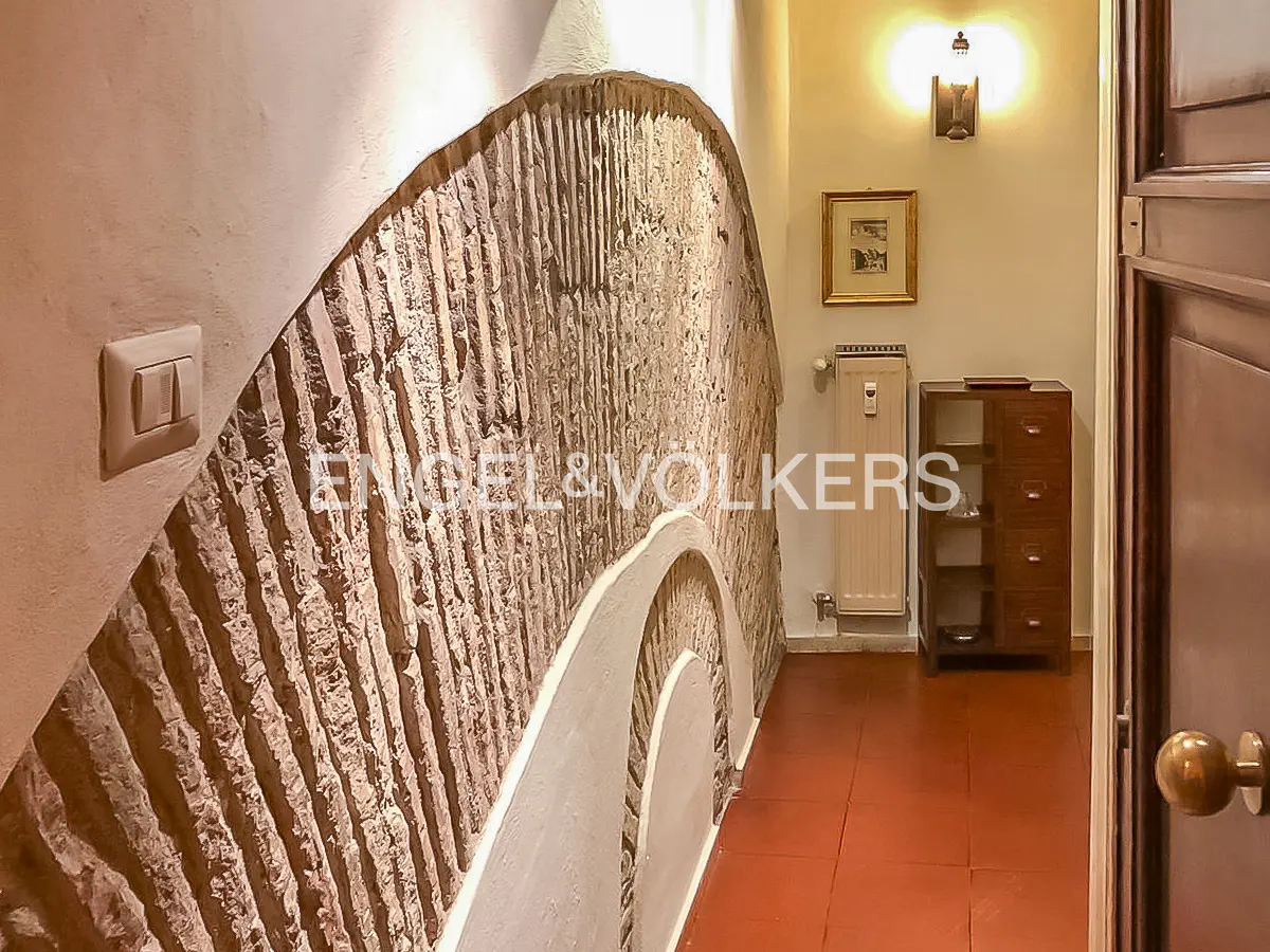 Interior view of a hallway with a textured stone wall, terracotta tile floor, and a wooden cabinet.