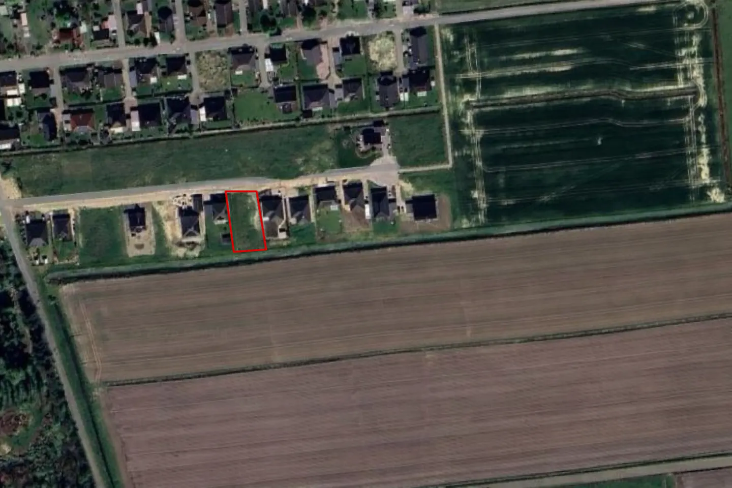 Aerial view of a vacant lot outlined in red, adjacent to houses and farmland.