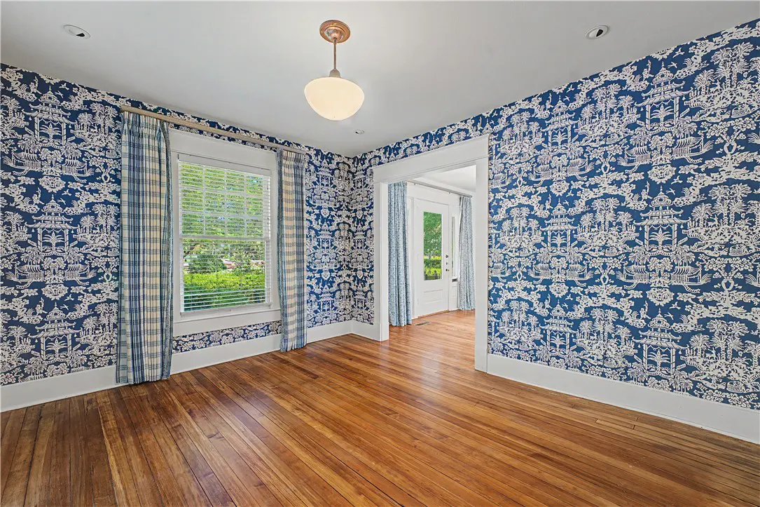 A room with blue and white wallpaper, hardwood floors, a window with plaid curtains, and a doorway.