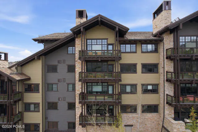 Exterior view of a multi-story condo building with balconies, stone accents, and a brown roof against a blue sky.