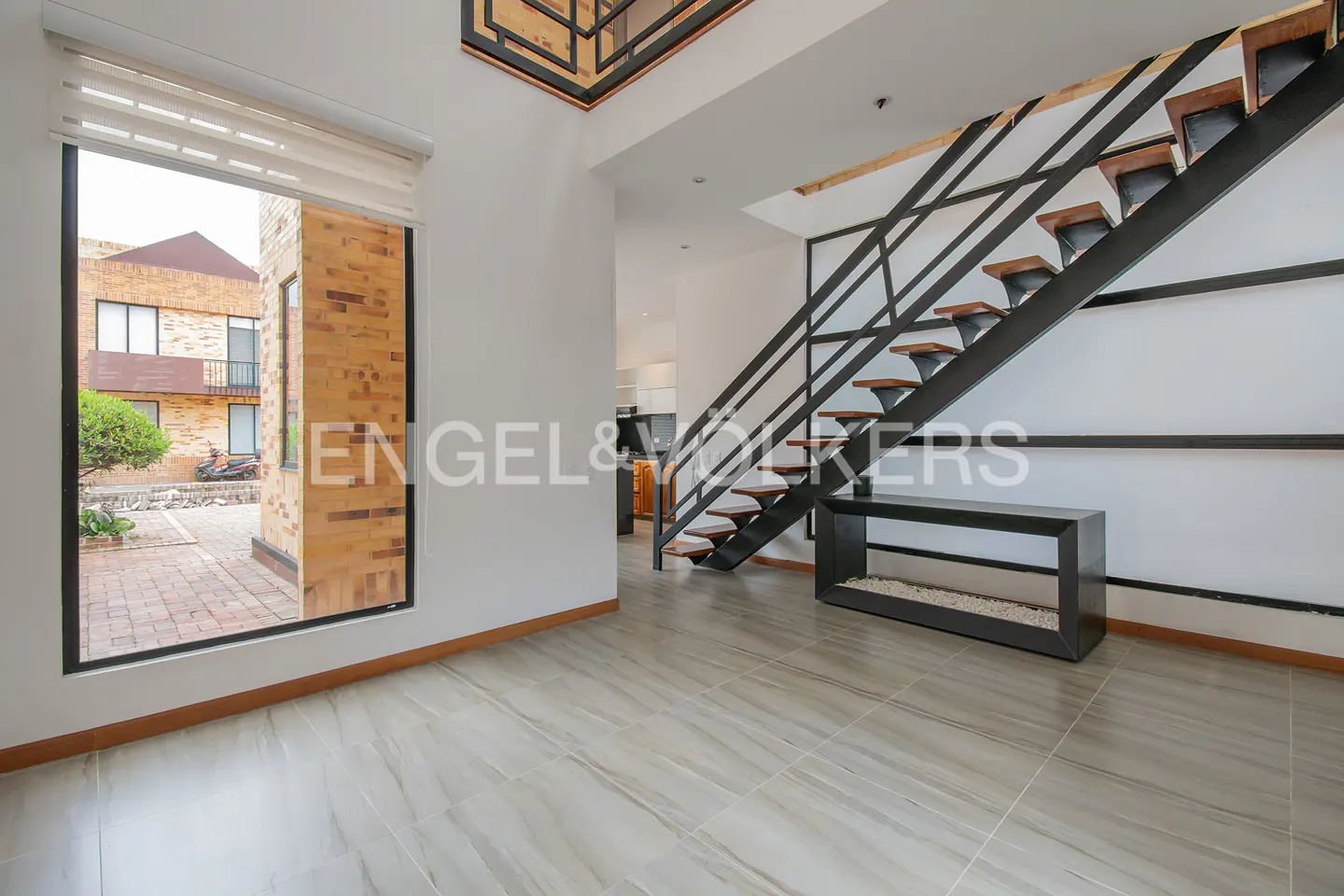 A modern living room with gray tile floors, a black staircase, and a large window.
