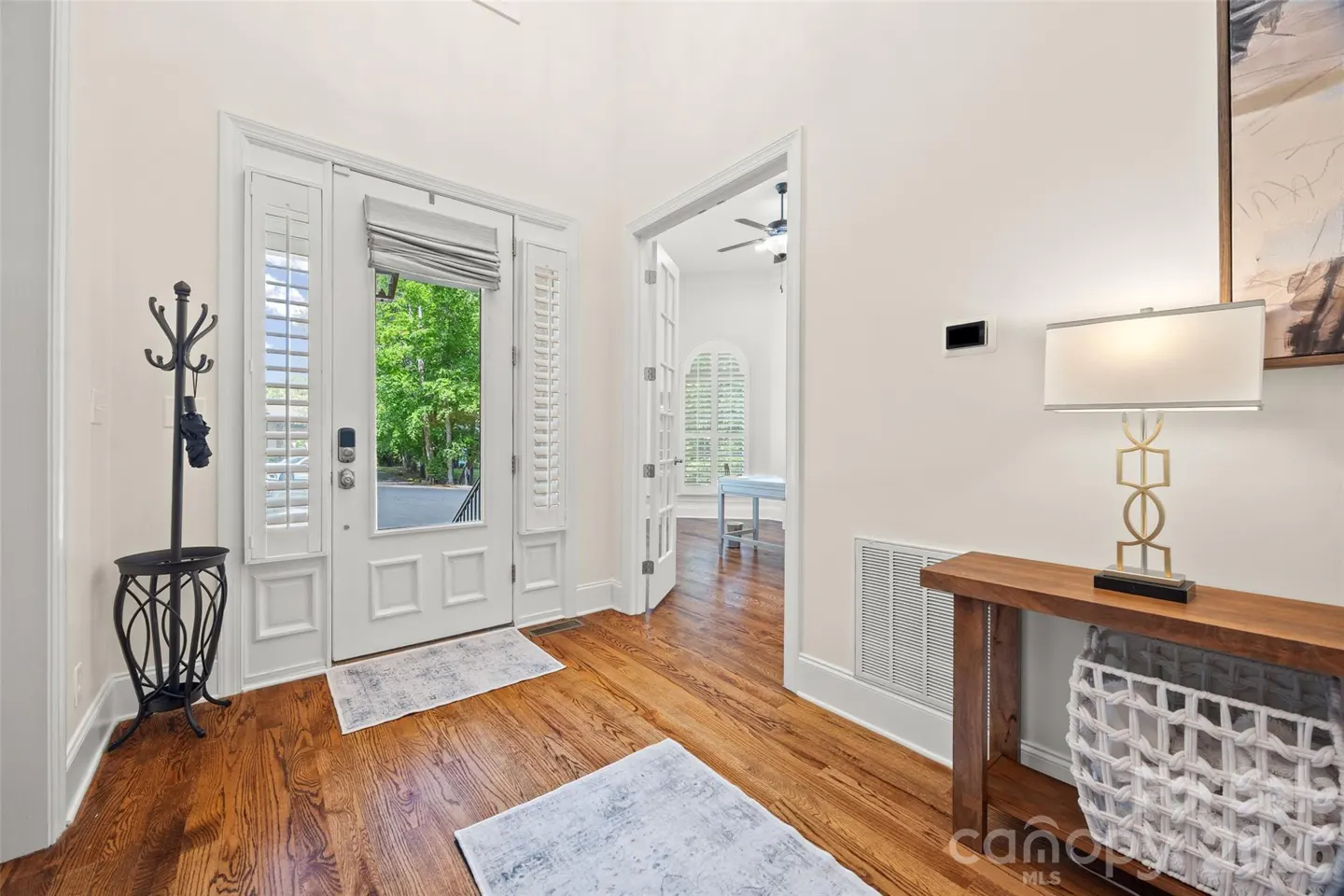 Bright entryway with hardwood floors, white front door with glass, coat rack, and a console table with a lamp.