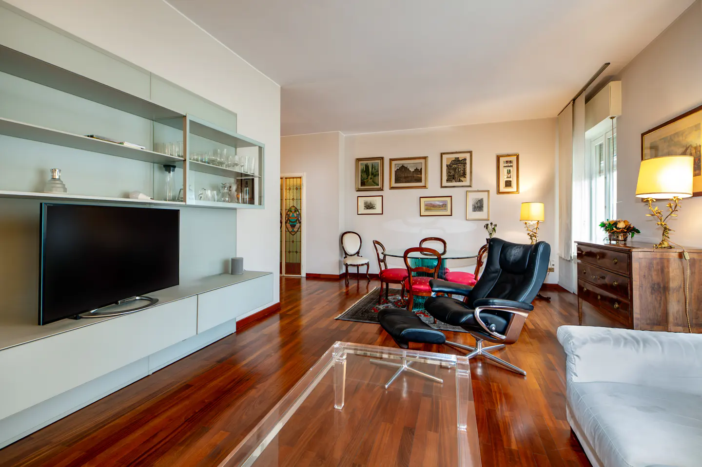 Living room with hardwood floors, a black leather chair, a glass table, and a TV on a light blue shelf.
