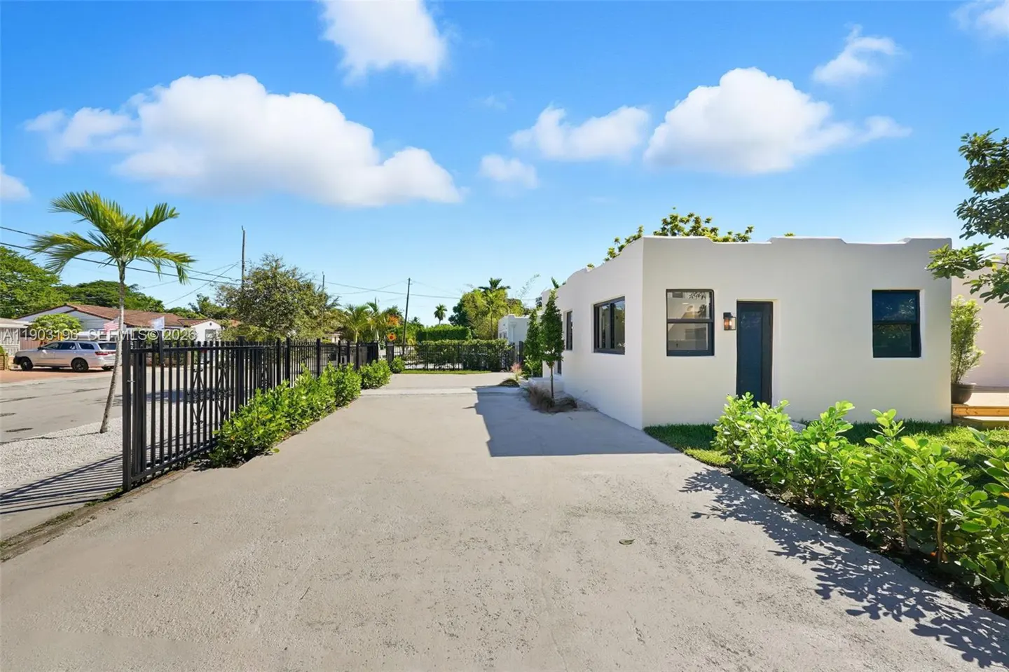 Exterior of a white, one-story home with a black door and window trim, a concrete driveway, and a black metal fence.