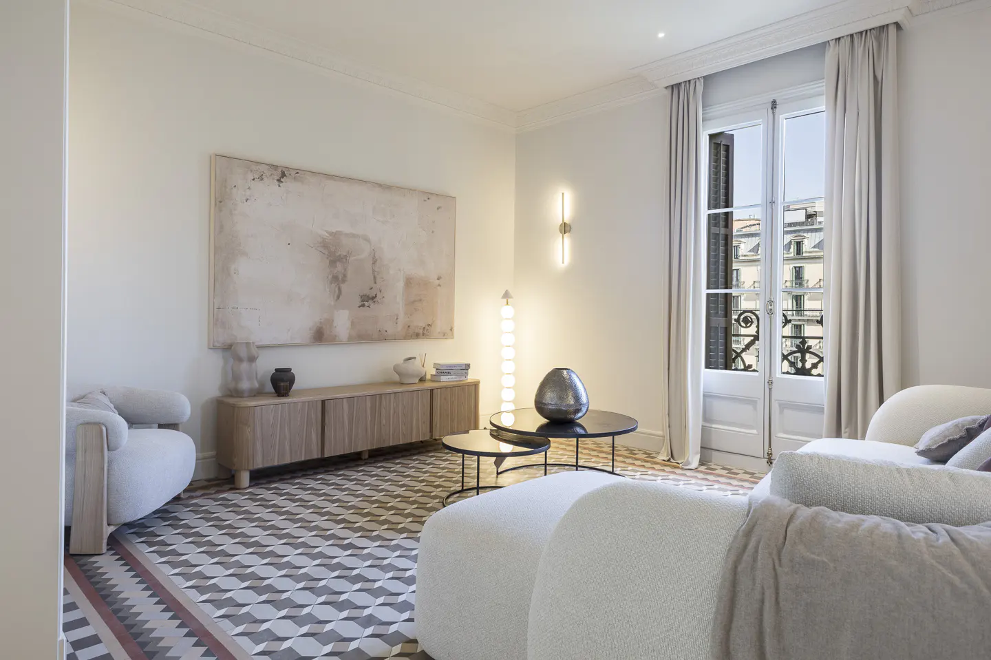 Bright living room with white sofa, patterned floor, and art. French doors open to a city view. Neutral tones create a serene atmosphere.