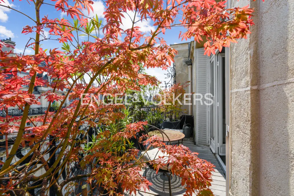 Balcony view with red Japanese maple tree, wrought iron railing, table, and white shuttered doors. Engel & Volkers logo visible.