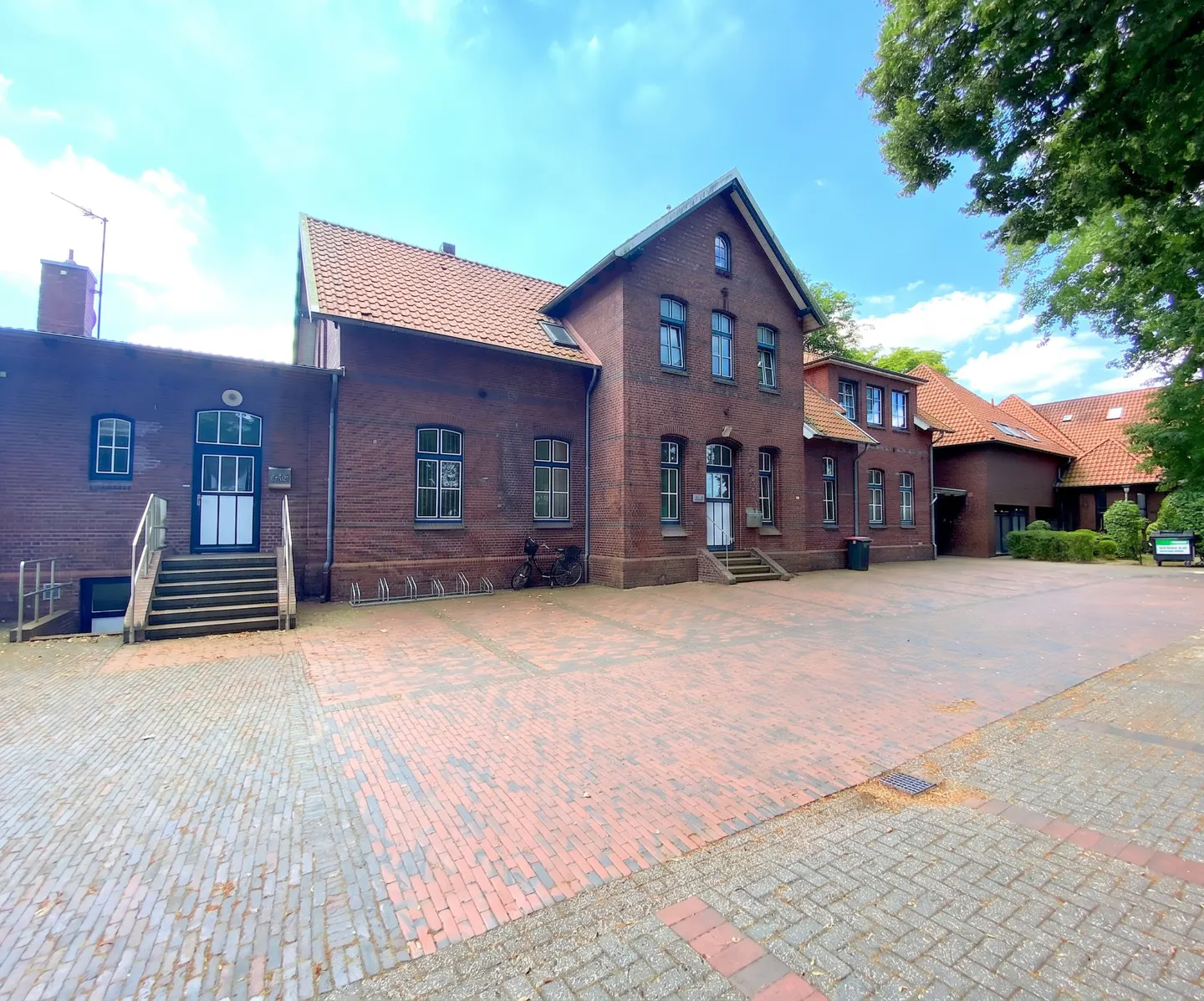 Exterior view of a red brick building with a red tile roof and a brick-paved courtyard.
