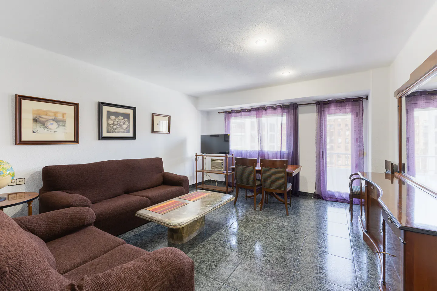 Living room with brown sofas, a marble coffee table, dining area, and purple curtains over a glass door and window.