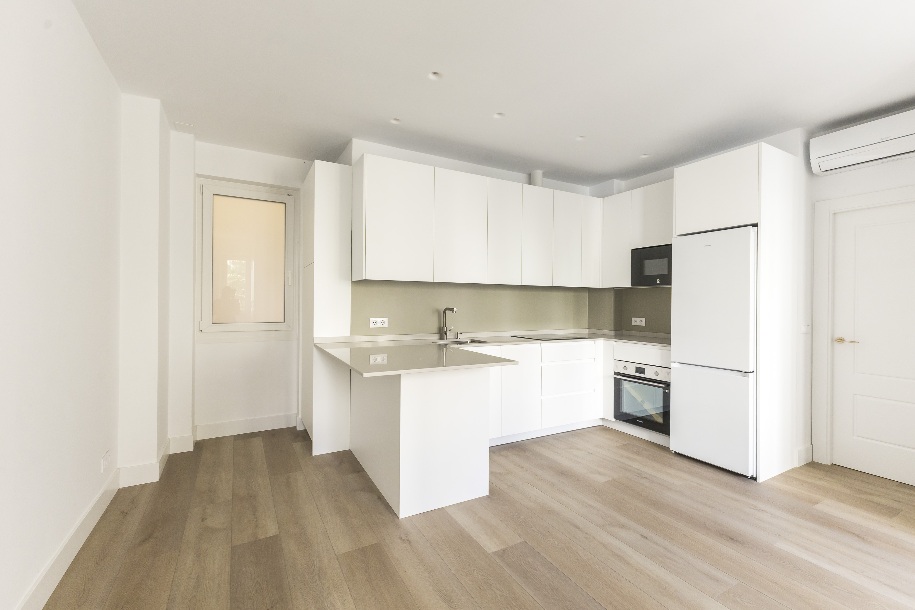 Modern kitchen with white cabinets, light wood floors, a small peninsula, and integrated white appliances.