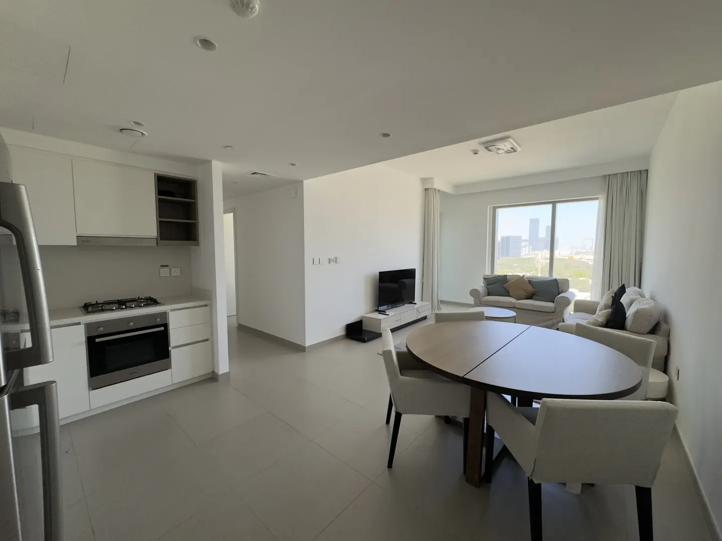 Bright, modern apartment interior with white walls, kitchen, dining table, and living room with city view.