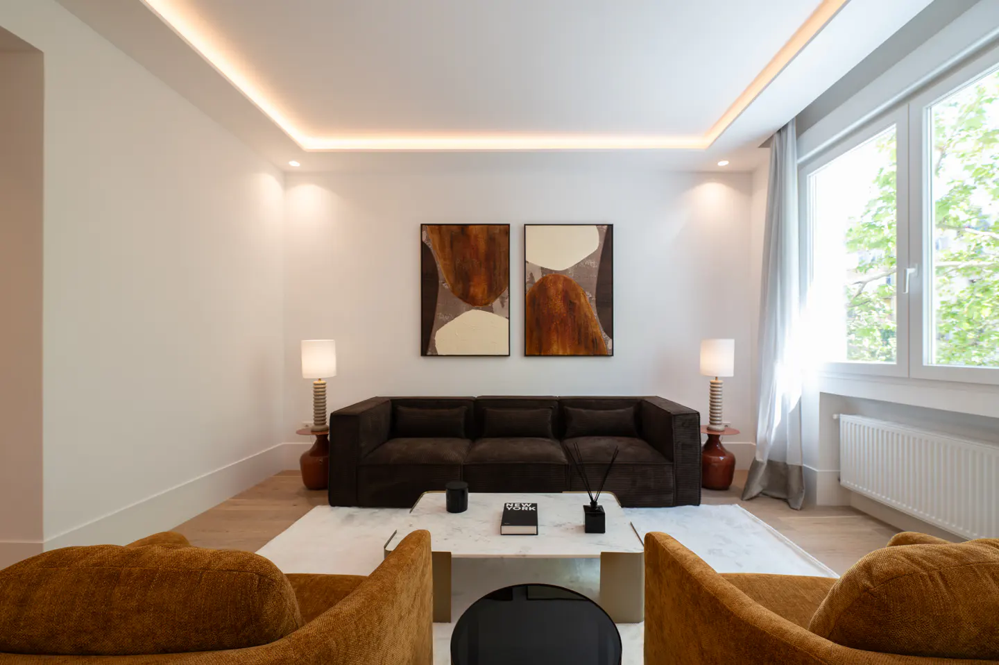 Living room with brown sofa, two orange chairs, marble coffee table, and two abstract paintings on the wall.