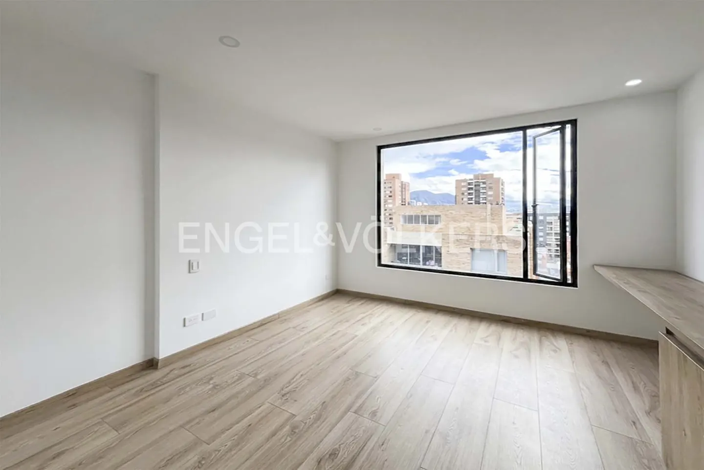 Bright, empty room with light wood floors, white walls, and a large window with a city view.
