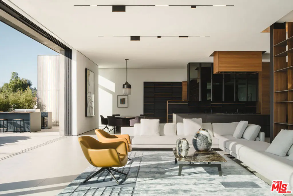 Bright, modern living room with white sofas, yellow chairs, and a marble coffee table on a blue rug. Open to an outdoor patio.