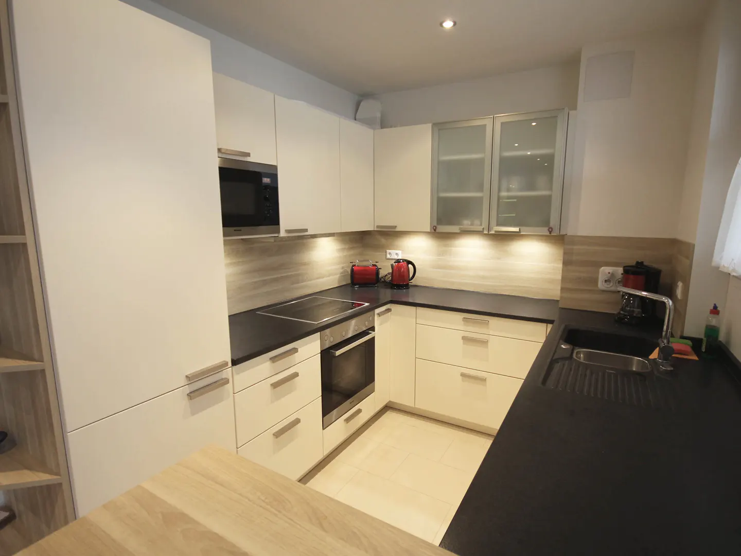 Bright kitchen with white cabinets, black countertops, and stainless steel appliances. A red toaster and kettle add a pop of color.