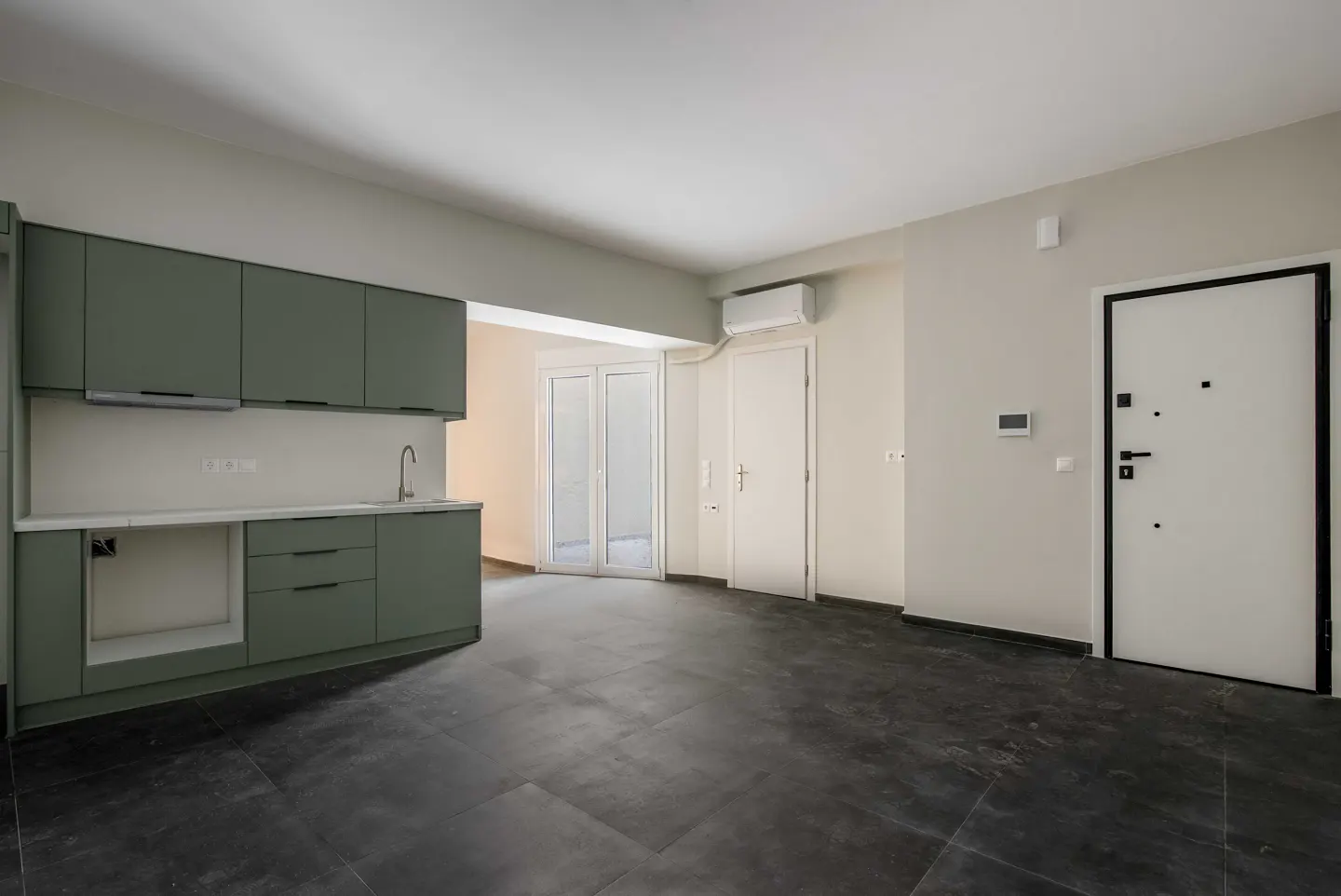 An empty room with dark tile floors, sage green kitchen cabinets, and a white door with a black frame.