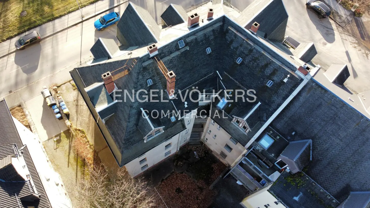 Aerial view of a commercial building with a dark gray roof, red brick chimneys, and the Engel & Völkers logo.