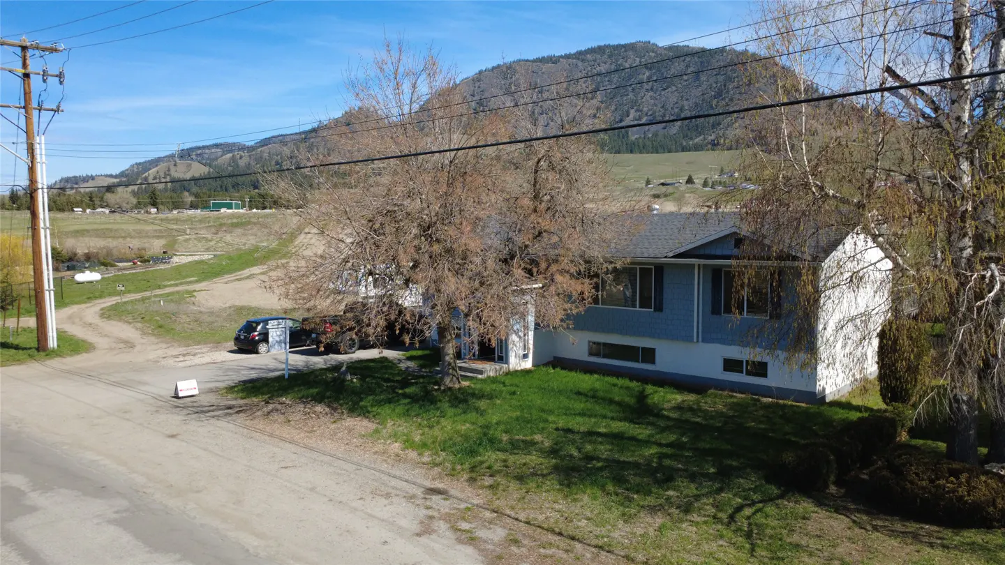 Two-story blue and white house with a gray roof, trees, and a mountain backdrop on a sunny day.
