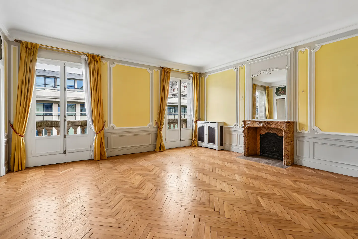 Bright living room with herringbone wood floors, yellow walls, ornate fireplace, and floor-to-ceiling yellow curtains.