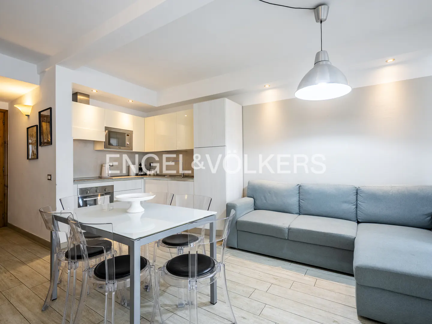 Open-concept living space with a white kitchen, dining table with clear chairs, and a blue sectional sofa.