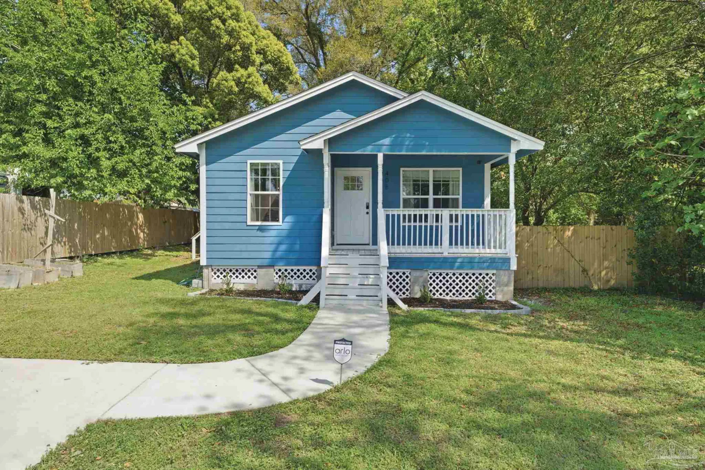 A blue, one-story house with a white porch and white trim is surrounded by green grass and trees.