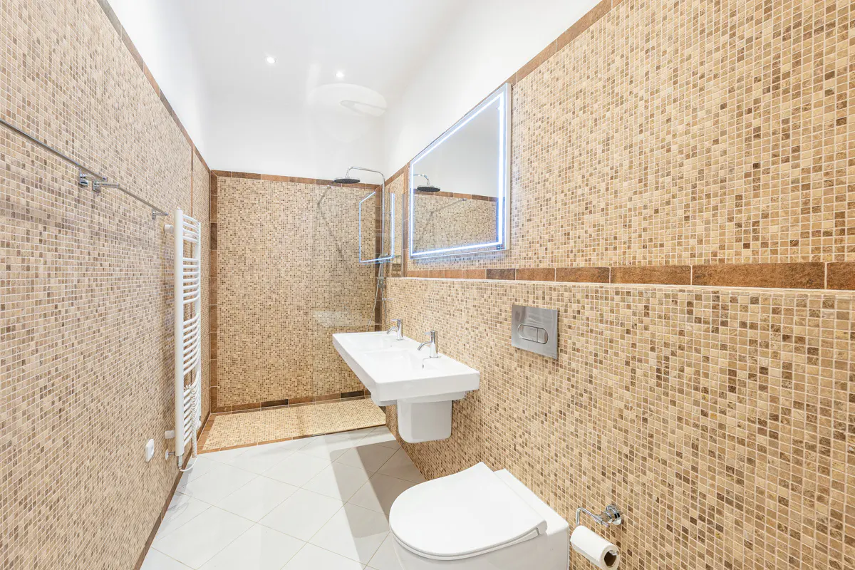 Bathroom with mosaic tile walls, white toilet, double sink, and shower. A heated towel rack is on the left wall.