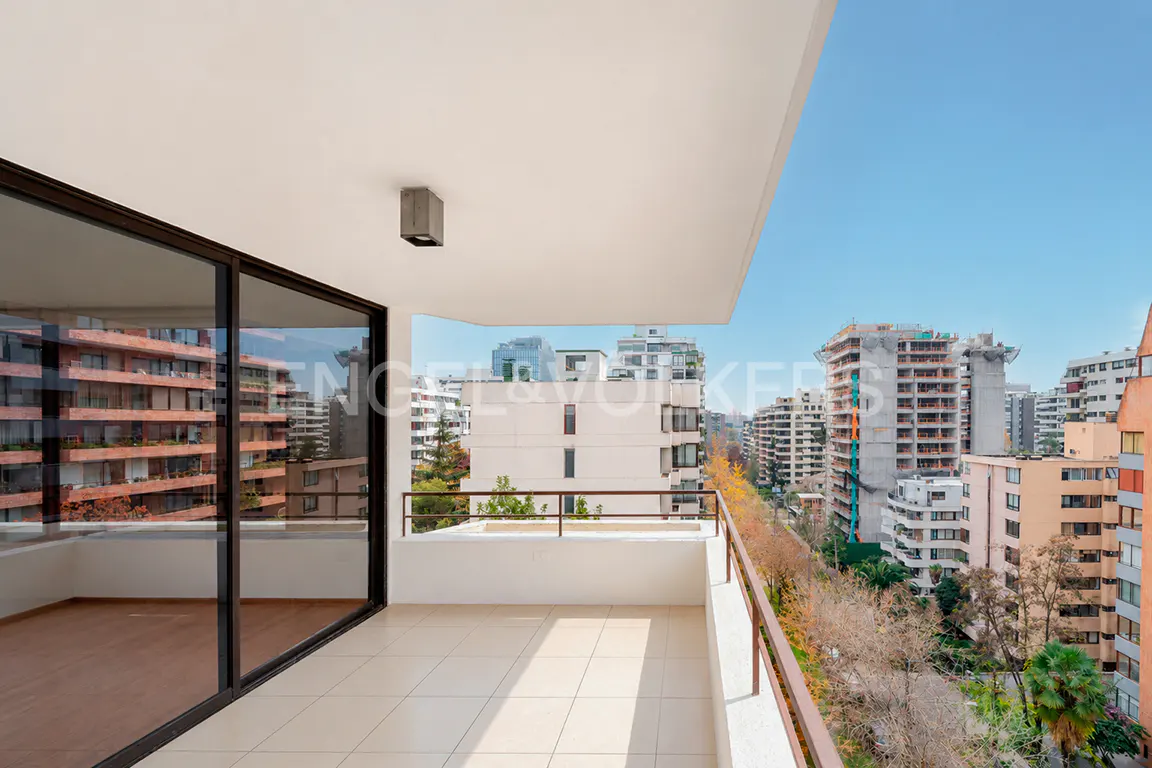 Modern apartment balcony with tiled floor, glass sliding doors, and a view of surrounding city buildings and trees.