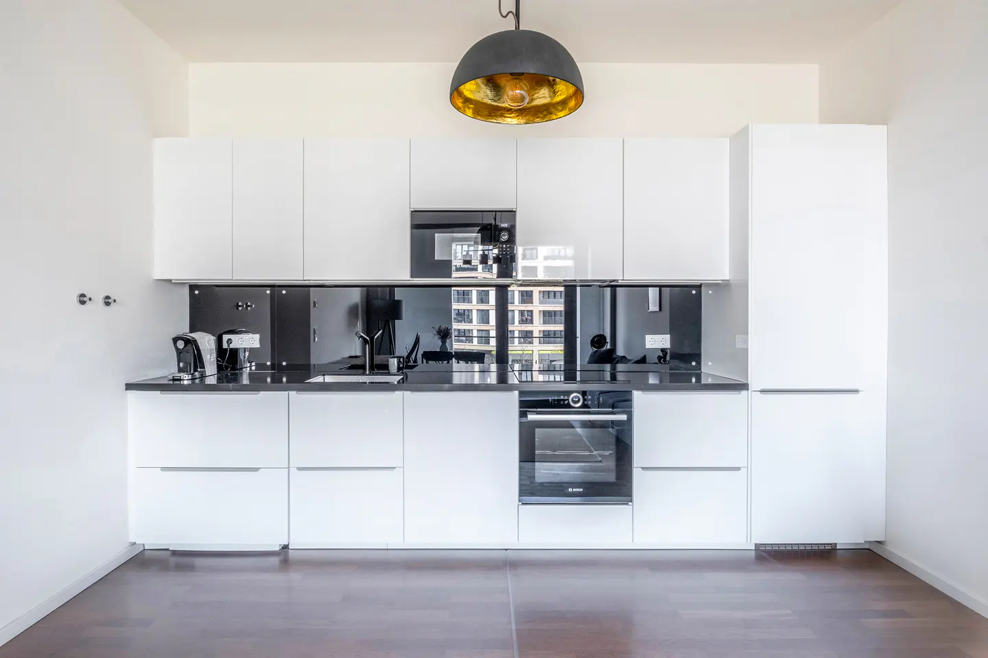 Modern kitchen with white cabinets, black countertop, and mirrored backsplash. A black pendant light hangs above.