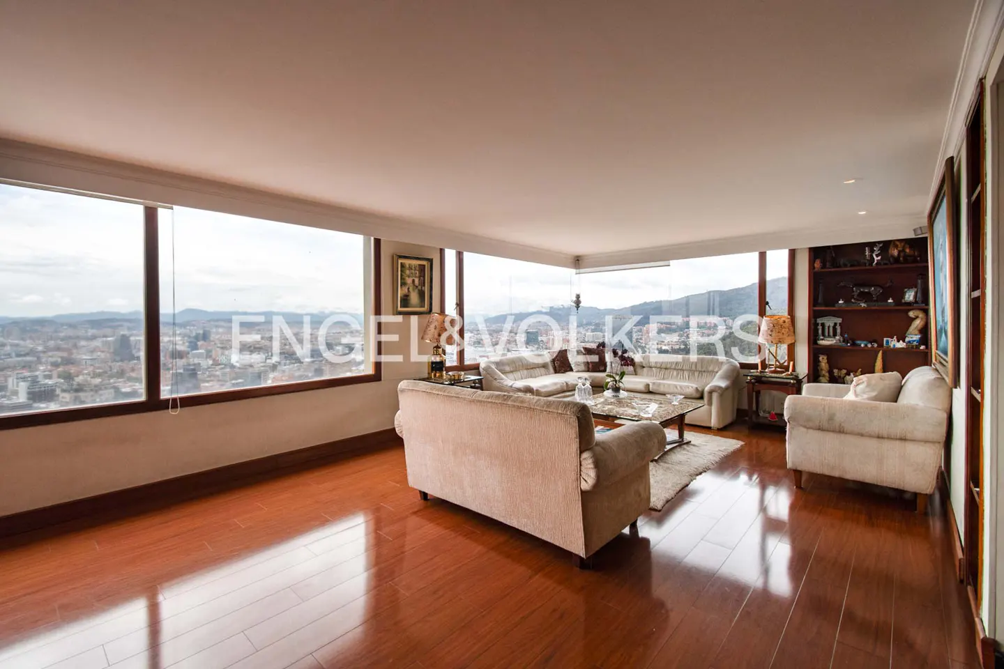 Living room with hardwood floors, beige sofas, and a large window overlooking a city.