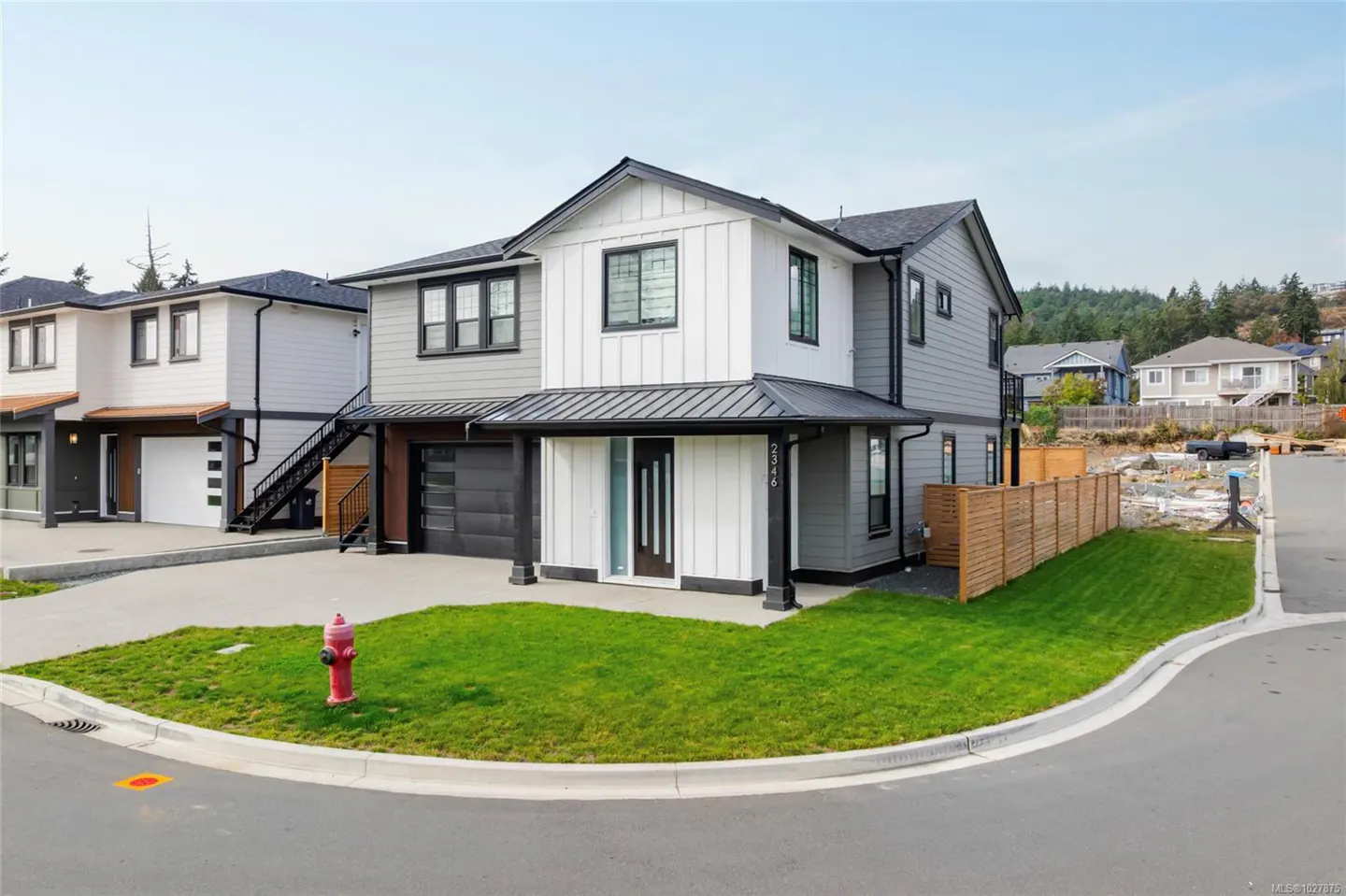 Two-story modern home with gray and white siding, black trim, and a black garage door. A red fire hydrant sits on the green lawn.