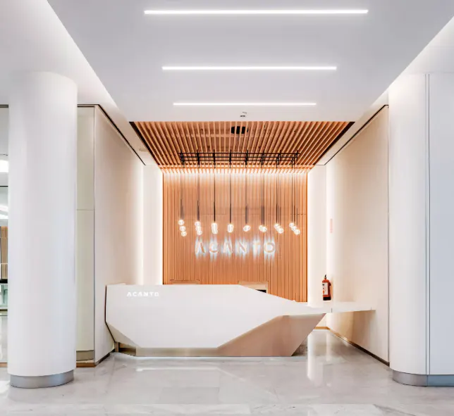 Modern office lobby with a white reception desk, wood slat wall, and neon "ACANTO" sign. White columns and marble floors add to the bright, minimalist design.